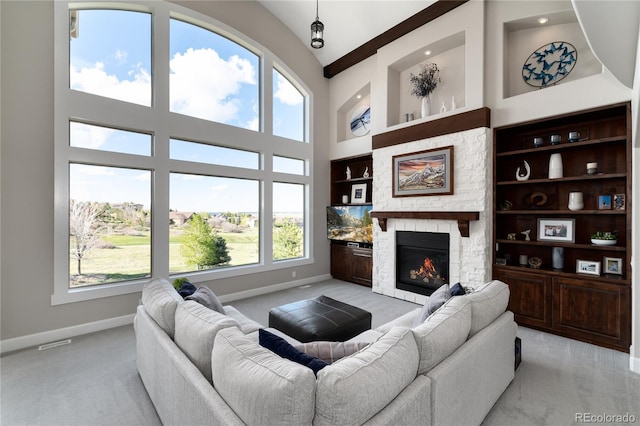 living area with baseboards, built in shelves, light carpet, a high ceiling, and a stone fireplace
