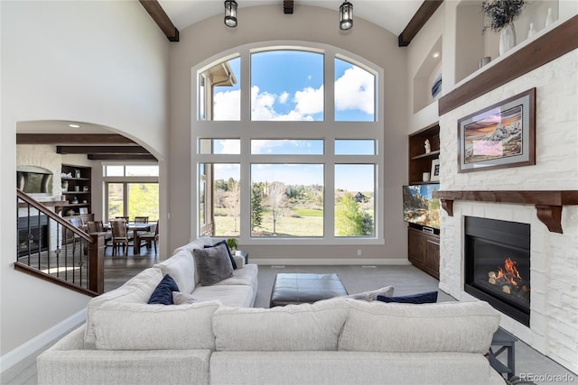 living area with a fireplace, baseboards, built in features, arched walkways, and a towering ceiling
