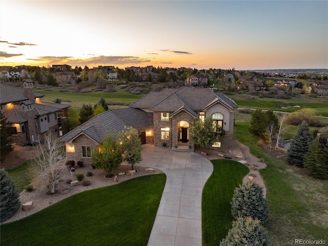 view of front of house with curved driveway, a tiled roof, a lawn, and stone siding