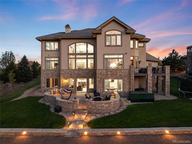back of house at dusk featuring a patio area, a trampoline, a lawn, and an outdoor living space with a fire pit