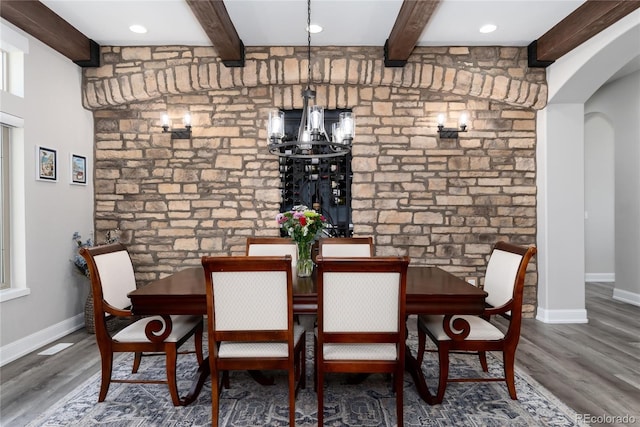 dining space with beamed ceiling, arched walkways, wood finished floors, baseboards, and a chandelier