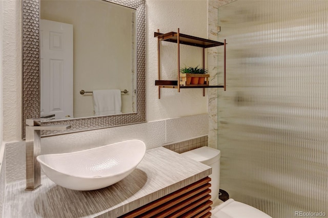 11358 W 85th Pl Unit E, Arvada, CO 80005 - bathroom with toilet, a textured wall, vanity, decorative backsplash, and tile walls