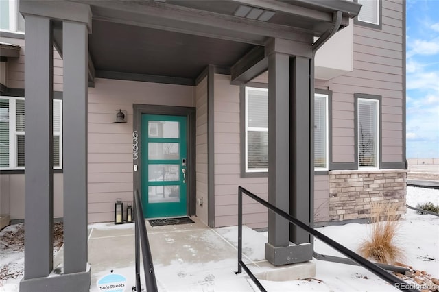 snow covered property entrance with stone siding