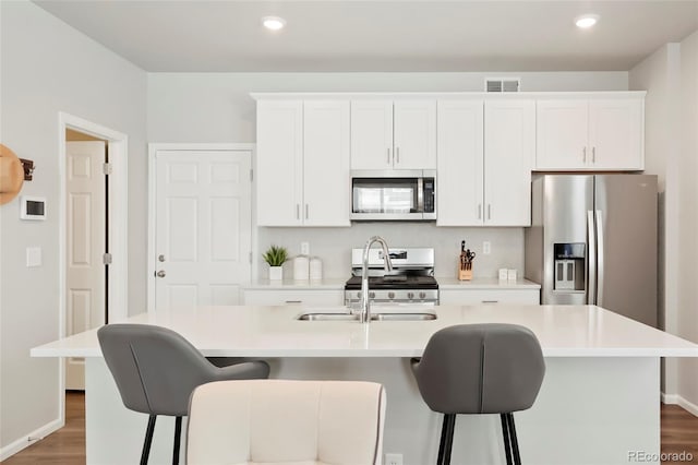 kitchen with stainless steel appliances, an island with sink, light countertops, and white cabinetry