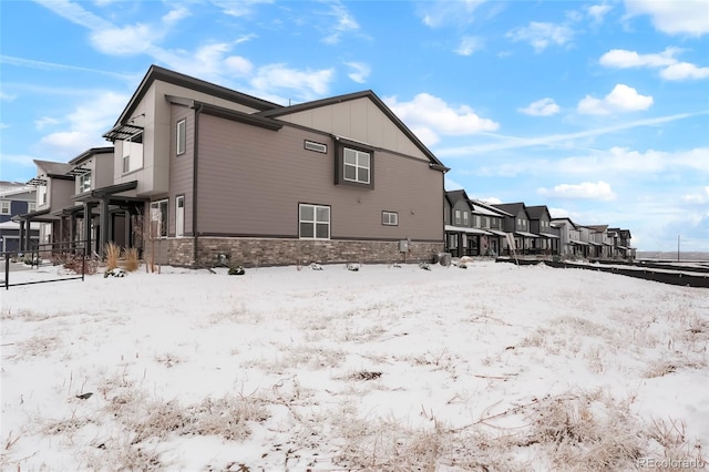 snow covered property featuring a garage, stone siding, a residential view, and board and batten siding