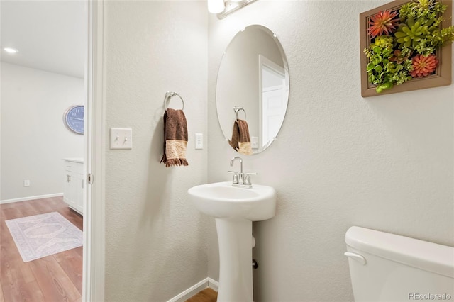 half bathroom with toilet, baseboards, a sink, and wood finished floors