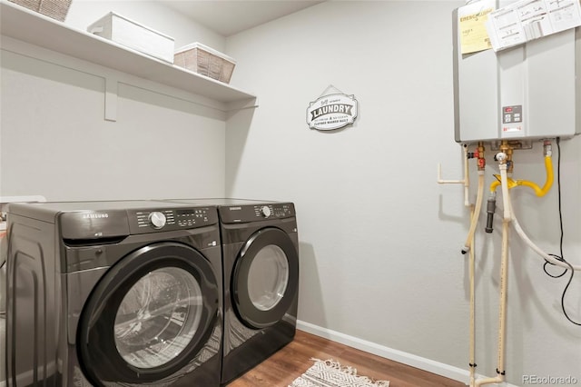 washroom with washing machine and clothes dryer, tankless water heater, wood finished floors, and baseboards