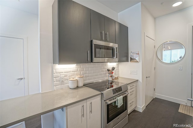 kitchen with dark wood-style flooring, stainless steel appliances, light countertops, decorative backsplash, and baseboards