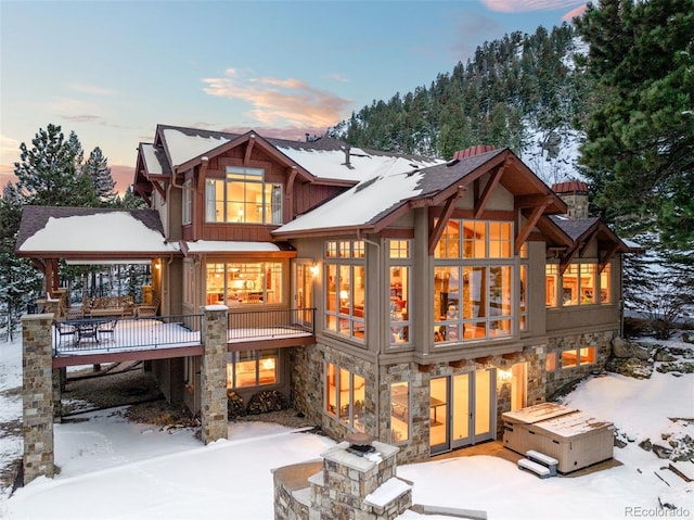 snow covered back of property featuring stone siding and a patio