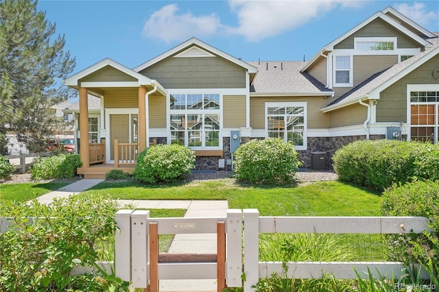 view of front of property with stone siding, a front yard, fence, and central air condition unit