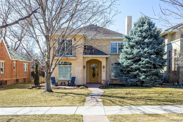 view of front of home with a chimney, stucco siding, a front yard, and a balcony