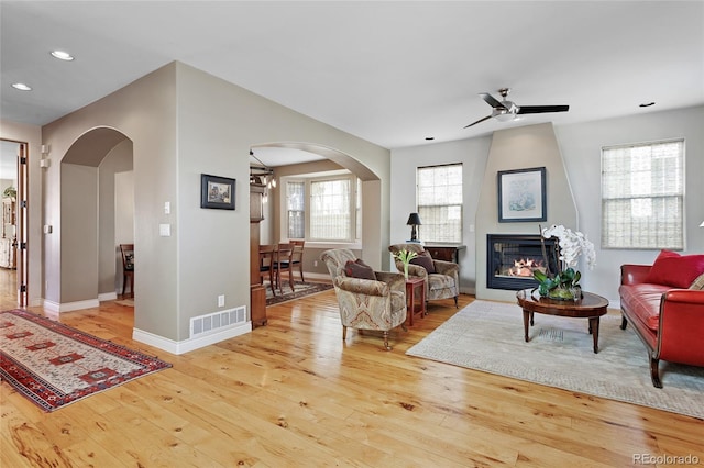 living room featuring light wood-type flooring, visible vents, arched walkways, and a large fireplace