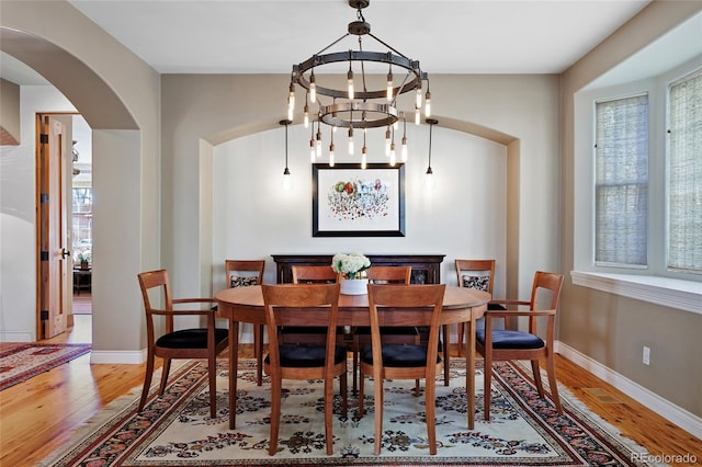 dining space featuring arched walkways, a notable chandelier, baseboards, and wood finished floors