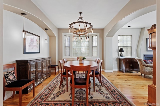 dining space featuring a notable chandelier, a glass covered fireplace, arched walkways, light wood-style floors, and baseboards