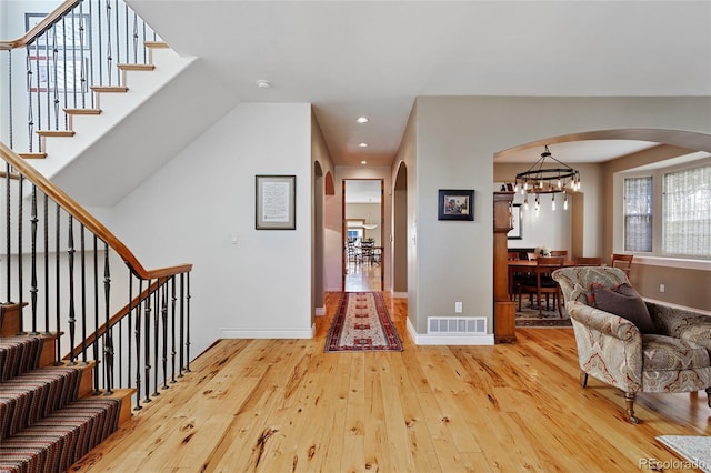 foyer with stairway, baseboards, visible vents, arched walkways, and light wood-type flooring