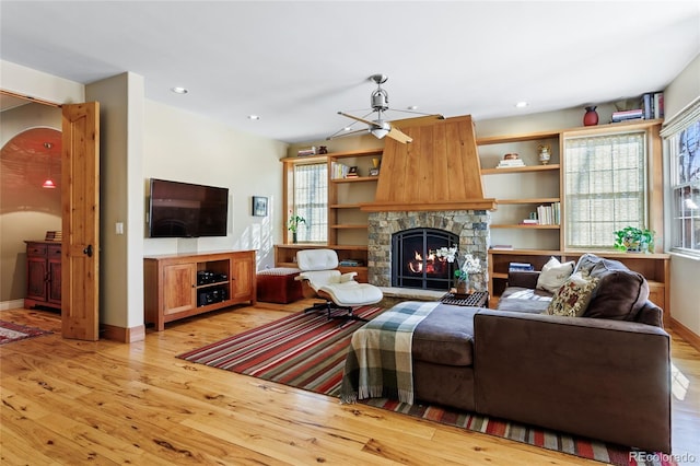 living room with plenty of natural light, a stone fireplace, light wood-style flooring, and a ceiling fan