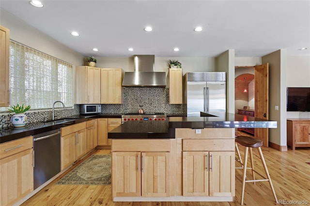 kitchen featuring a sink, appliances with stainless steel finishes, wall chimney exhaust hood, and light brown cabinetry