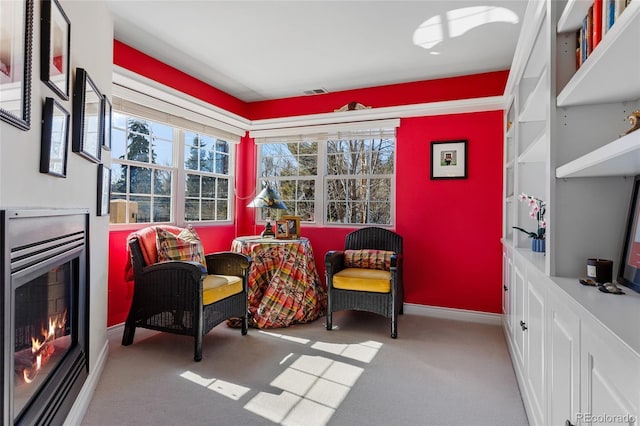 living area featuring visible vents, carpet, baseboards, and a warm lit fireplace