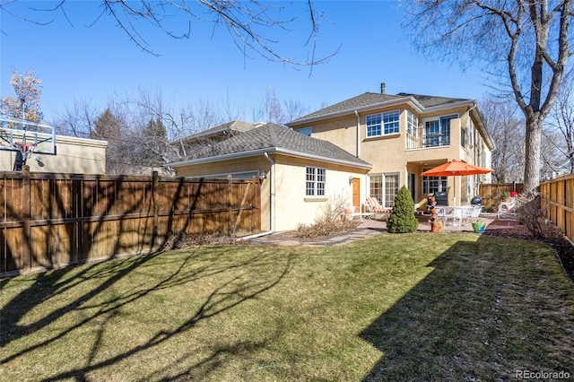 rear view of property with stucco siding, a lawn, a patio, a fenced backyard, and roof with shingles