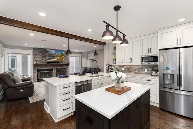 kitchen with a sink, beamed ceiling, open floor plan, and stainless steel appliances