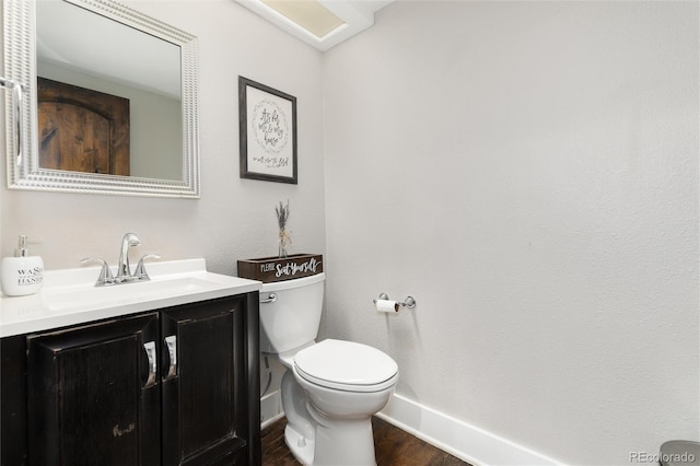 half bathroom with vanity, toilet, wood finished floors, and baseboards