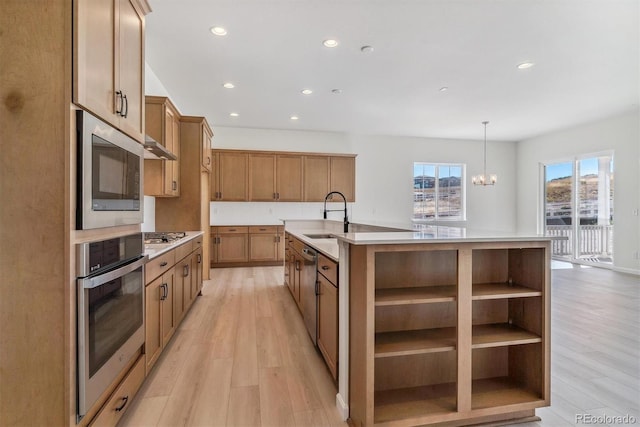 kitchen with decorative light fixtures, stainless steel appliances, a kitchen island with sink, and sink