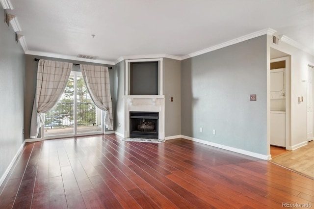 unfurnished living room with crown molding, stacked washing maching and dryer, and wood-type flooring