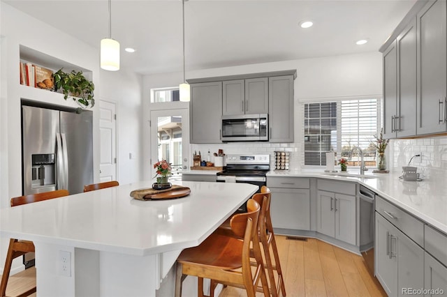 kitchen featuring stainless steel appliances, gray cabinets, a sink, and a kitchen bar