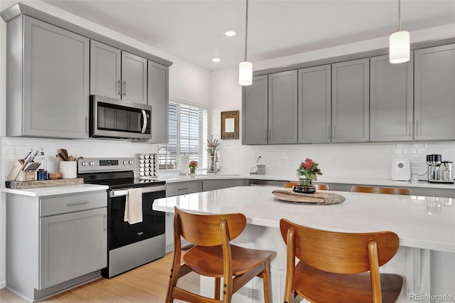 kitchen with stainless steel appliances, gray cabinets, light countertops, and a kitchen breakfast bar