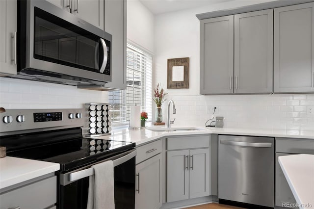 kitchen with a sink, light countertops, appliances with stainless steel finishes, gray cabinets, and decorative backsplash