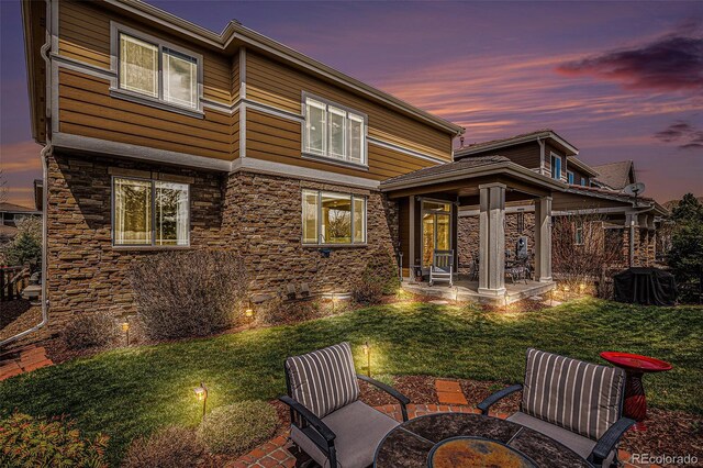 7004 S Addison Ct, Aurora, CO 80016 - back of property at dusk featuring stone siding, a lawn, an outdoor fire pit, and a patio