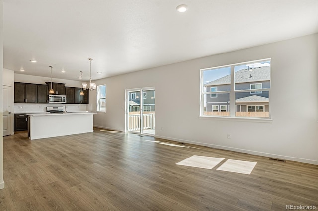 unfurnished living room featuring baseboards, an inviting chandelier, recessed lighting, and wood finished floors