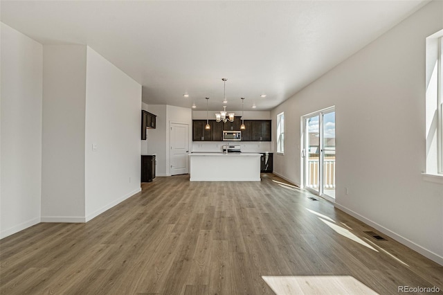 unfurnished living room featuring baseboards, a chandelier, wood finished floors, and visible vents