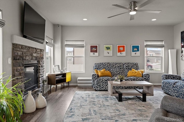 living room featuring baseboards, a stone fireplace, a healthy amount of sunlight, and wood finished floors