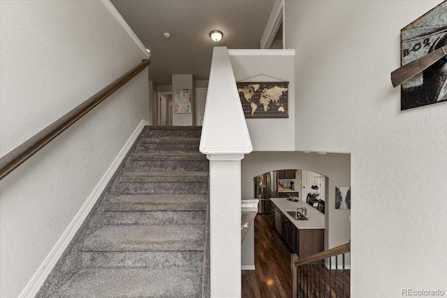 staircase with wood finished floors, baseboards, arched walkways, and a textured wall