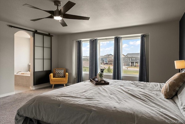 carpeted bedroom with connected bathroom, a textured ceiling, a barn door, and arched walkways