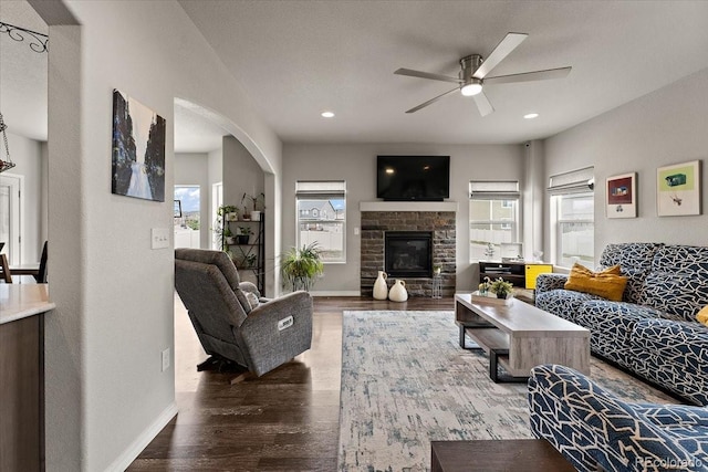 living room with wood finished floors, a fireplace, ceiling fan, arched walkways, and baseboards
