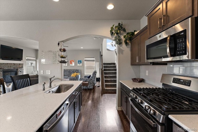 kitchen with dark wood finished floors, a sink, dark brown cabinetry, open floor plan, and stainless steel appliances