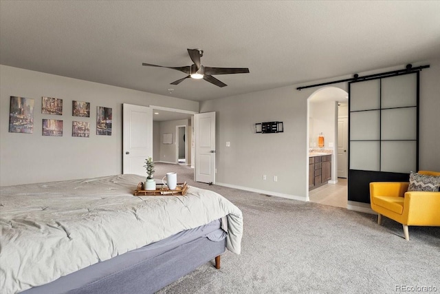 bedroom featuring ensuite bathroom, a barn door, light carpet, arched walkways, and baseboards