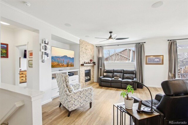 living room featuring baseboards, a fireplace, a ceiling fan, and light wood-style flooring