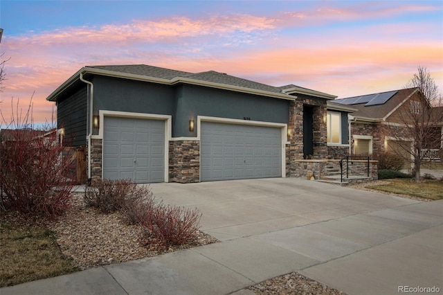 prairie-style house featuring a garage, stucco siding, driveway, and stone siding