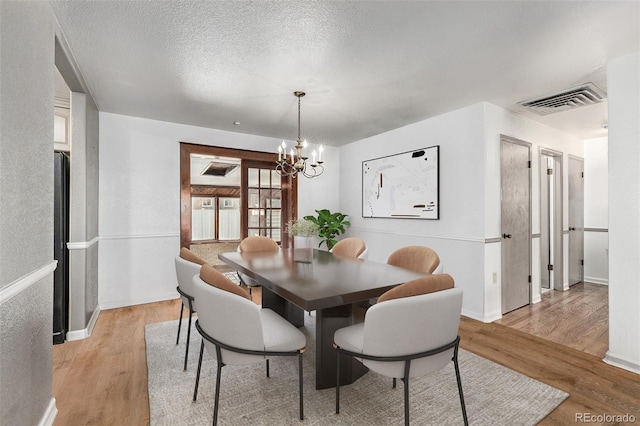 dining room with a textured ceiling, light hardwood / wood-style flooring, and a notable chandelier