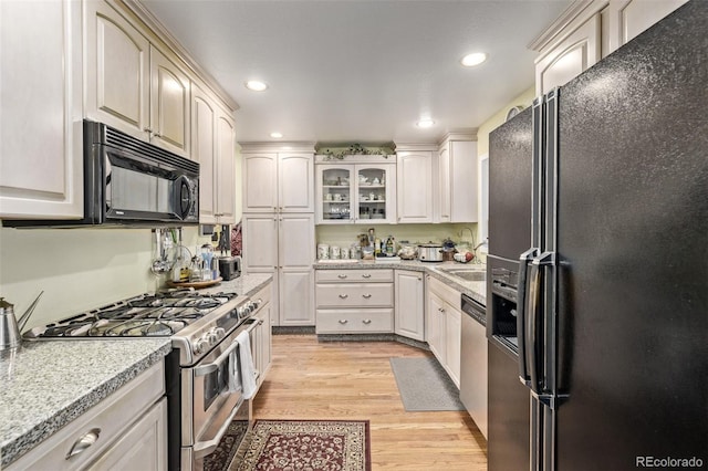 kitchen with light stone counters, sink, black appliances, and light wood-type flooring