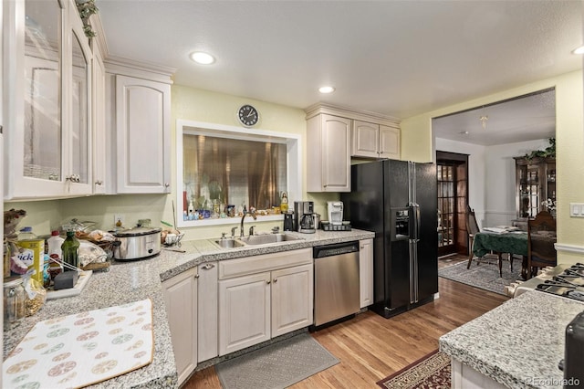 kitchen with white cabinetry, sink, stainless steel dishwasher, black refrigerator with ice dispenser, and light hardwood / wood-style flooring