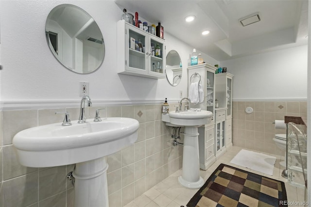 bathroom with tile patterned flooring, dual sinks, tile walls, and toilet