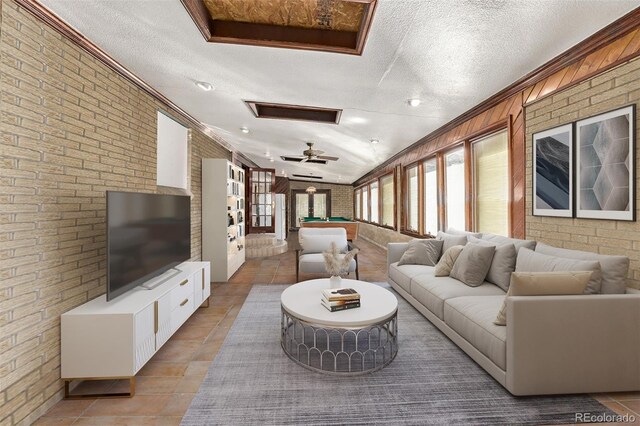 living room featuring ceiling fan, light tile patterned flooring, a textured ceiling, and brick wall