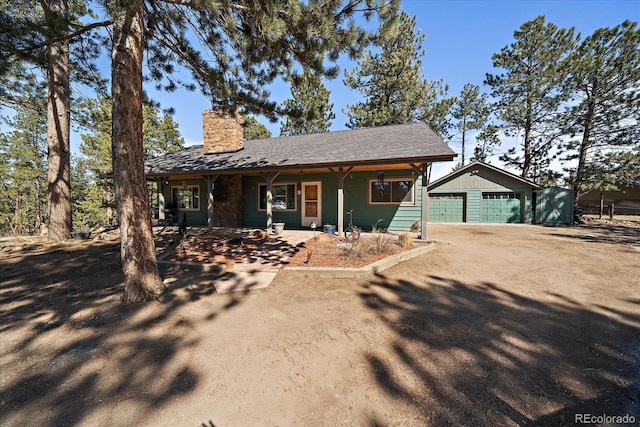 view of front of home featuring an outbuilding, a porch, a chimney, and a garage