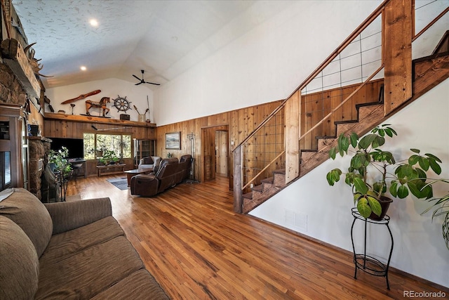 living area with high vaulted ceiling, a fireplace, ceiling fan, stairs, and hardwood / wood-style flooring