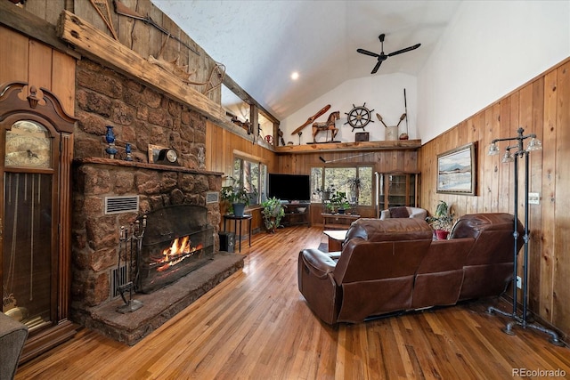 living room with wood walls, a fireplace, a ceiling fan, and wood finished floors