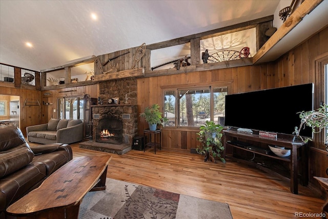 living area with a stone fireplace, vaulted ceiling, wooden walls, and wood finished floors